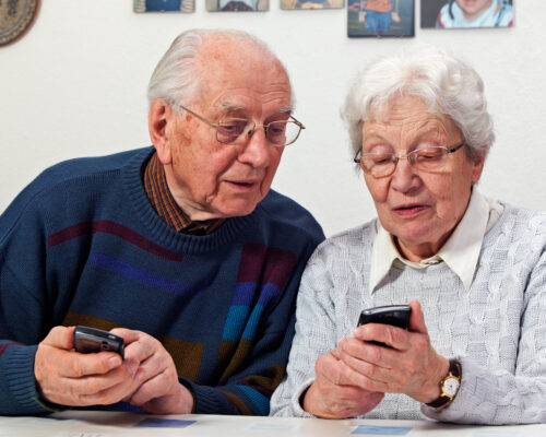Ein älterer Mann und eine ältere Frau sitzen nebeneinander und tippen auf ihre Smartphones.