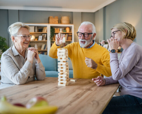 Zwei Seniorinnen und ein Senior spielen gemeinsam mit Holzbauklötzen und bauen einen Turm. A